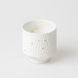 Rundes Windlicht aus weißem Porzellan mit Hammerschlag-Optik und goldenen Sternen.