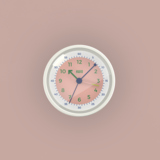 Runder Wecker mit rosafarbenem Ziffernblatt und grünen Ziffern auf hellem Hintergrund.