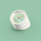 Wecker mit buntem Ziffernblatt und farbigen Zeigern auf grünem Hintergrund.