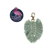 Zwei Accessoires für einen Rucksack: ein Flamingo-Patch und eine grüne Quasten-Anhängerkette.