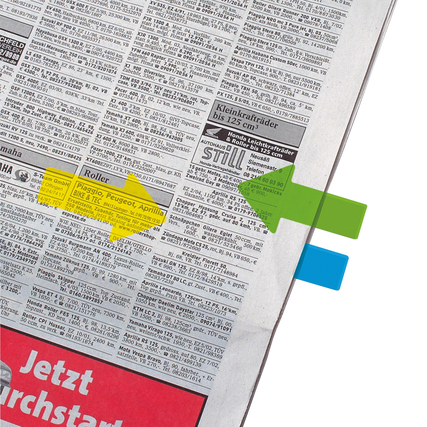 Transparente Haftstreifen in grüner und gelber Pfeilform markieren Textstelle in einer Zeitung.