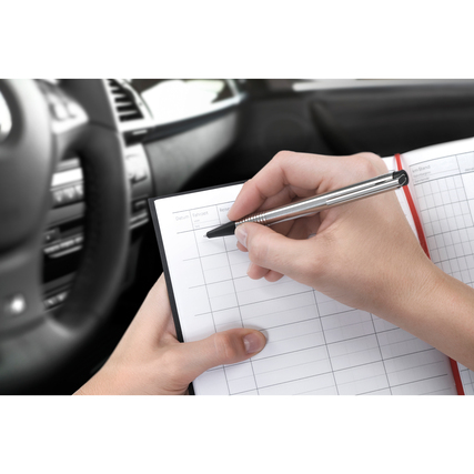 Hand, die in einem Fahrzeug ein Fahrtenbuch ausfüllt, im Hintergrund das Armaturenbrett sichtbar.