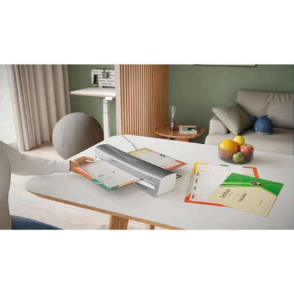 Laminiergerät in Gebrauch auf einem Tisch mit Dokumenten und Dekoration im Hintergrund.