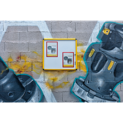 Schaukasten mit gelbem Rahmen an einer grauen Wand, zeigt zwei DIN A4 Dokumente.