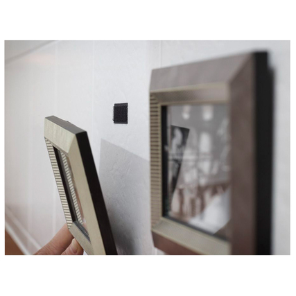 Schwarzes Klettquadrat wird zur Befestigung eines Bilderrahmens an einer Wand verwendet.