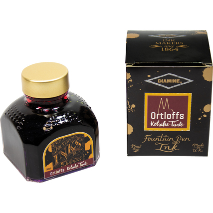 Rotes Tintenglas mit goldener Kappe und schwarz-goldener Verpackung.