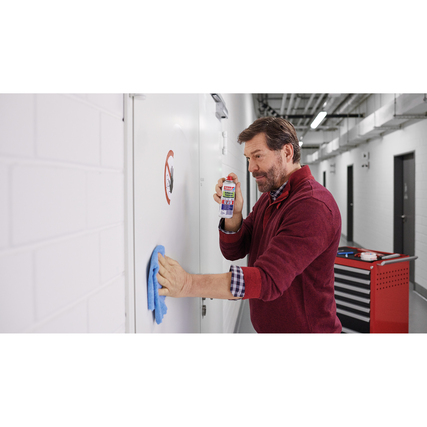 Mann verwendet Klebstoffentferner-Spray und wischt mit einem Tuch an einer Wand.