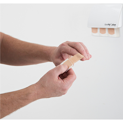 Mann zieht ein Pflaster aus dem QuickFix Pflasterspender an einer Wand.