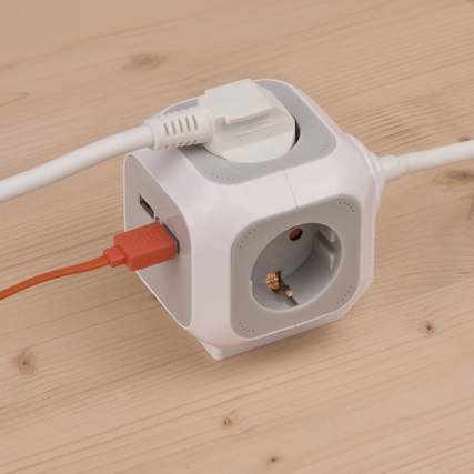 Steckdosenwürfel mit vier Steckdosen und zwei USB-Ladebuchsen auf einem Holztisch.