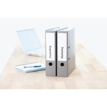 Zwei graue Ordner mit weißen Etiketten auf einem Tisch, Laptop und Notizblock im Hintergrund.