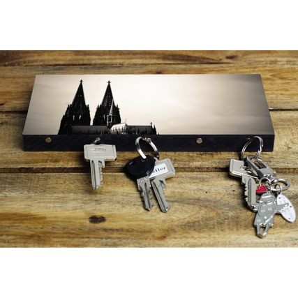 Schlüsselbrett mit Kölner Dom-Motiv und mehreren Schlüsseln auf einer Holzoberfläche.