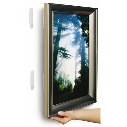 Hand, die ein Bilderrahmen mit Command Klebepad an einer Wand anbringt.