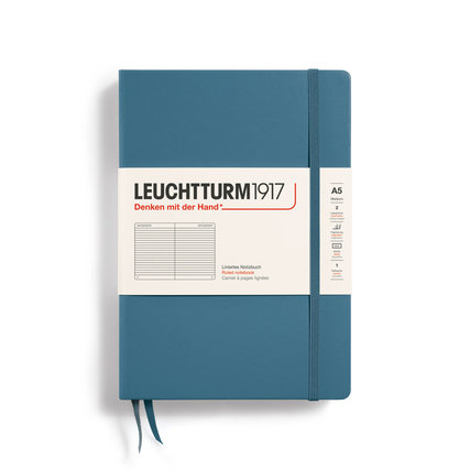 Hartcover-Notizbuch in stone blue mit Gummiband und einem beschrifteten Umschlag.