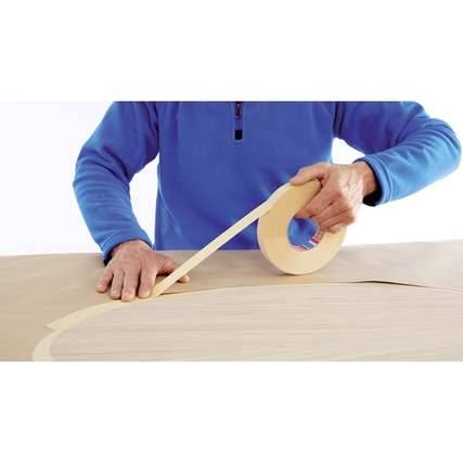 Person zieht ein Kreppband von einer Rolle auf eine Oberfläche, um eine Kurve abzukleben.