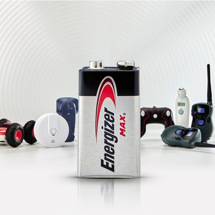 Batterie im AA-Format steht vor verschiedenen elektronischen Geräten auf hellem Hintergrund.