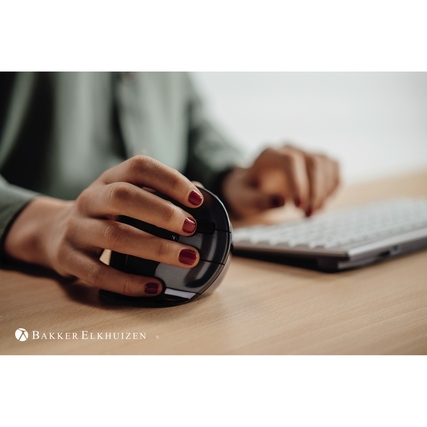Ergonomische vertikale PC-Maus in der Hand einer Person neben einer Tastatur auf einem Tisch.