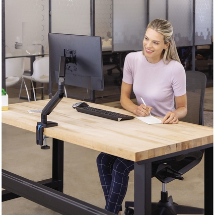 Monitorschwenkarm in Schwarz, montiert an einem Schreibtisch mit einem Laptop und Notizblock.