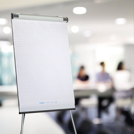 Kariertes Flipchartpapier auf einem Ständer in einem unscharfen Besprechungsraum.