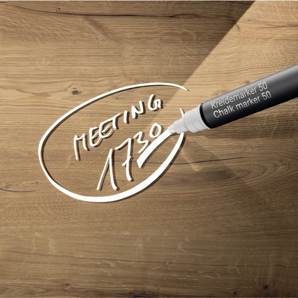 Glasboard mit beschriftetem Text "MEETING 1730" auf Holzhintergrund und Kreidemarker sichtbar.