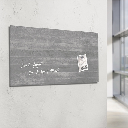 Hochglänzendes Glasboard in Sichtbetonoptik mit Notiz und Magneten an einer Wand gezeigt.