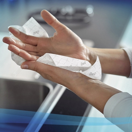 Hände halten ein Scott® Papierhandtuch über einem Waschbecken zur Demonstration der Anwendung.