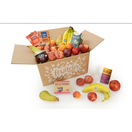 Pappkarton gefüllt mit verschiedenen Früchten, Snacks und Getränken.