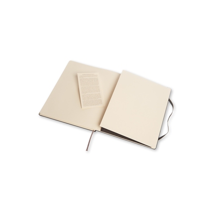 Offenes schwarzes Moleskine Notizbuch mit anliegendem Informationsblatt in neutralem Umfeld.