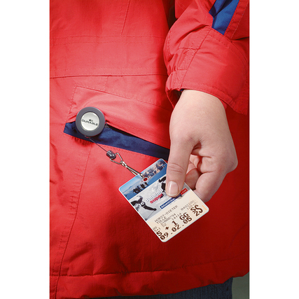 Jojo mit Krokoklemme und Federhaken hält eine Namensschildkarte, gezeigt an roter Jacke.