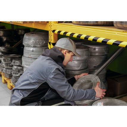 Mitarbeiter im Lager verwendet ein Eckschutzprofil an einem Regal zur Gefahrenmarkierung.