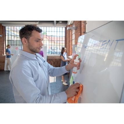 Person reinigt ein Whiteboard mit einem Tuch und einem Reinigungsmittel in einem Büro.