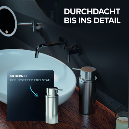 Freistehender silberner Seifenspender aus gebürstetem Edelstahl vor einem Waschbecken.