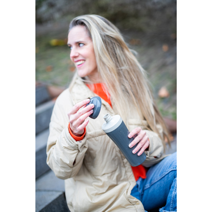 Graue Trinkflasche mit abnehmbarem Verschluss, gehalten von einer Person im Freien.