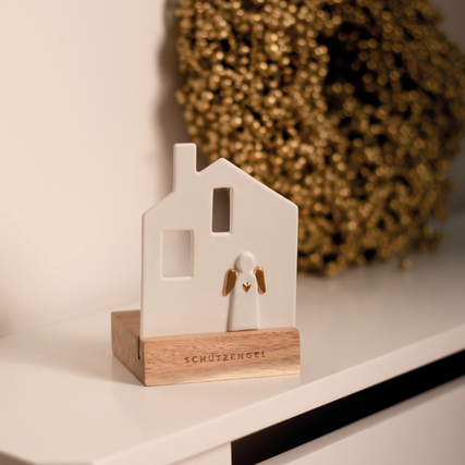 Weißer Teelichthalter in Form eines Hauses mit Engel aus Holzsockel und goldenen Akzenten.