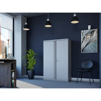 Grauer Flügeltürenschrank steht in einem modern eingerichteten Büro mit Pflanzen und Möbeln.