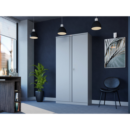 Grauer Flügeltürenschrank steht in einem modernen Büro mit Pflanzen und Möbeln im Hintergrund.
