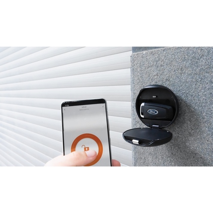 Smart-Key-Safe an einer Wand mit Smartphone zur Steuerung und geöffnetem Fach für Schlüssel.