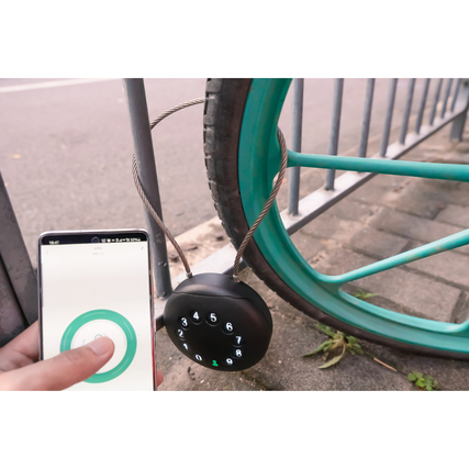 Schlüsselbox mit Kabel an einem Fahrradrahmen, während ein Smartphone zur Steuerung verwendet wird.