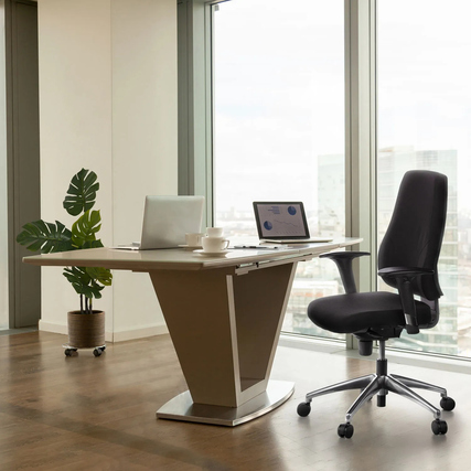 Schwarzer Bürodrehstuhl vor einem modernen Tisch in einem hellen Büro mit großen Fenstern.