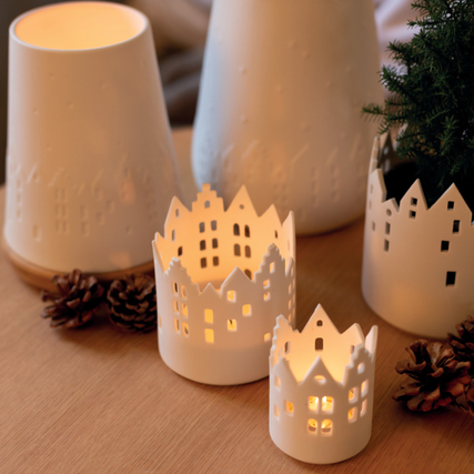 Teelichthalter in Form von Häusern mit warmem Licht und weihnachtlichen Motiven auf einem Tisch.