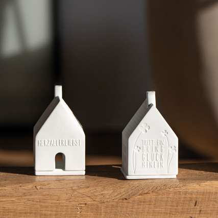 Zwei weiße Teelichthäuser mit geprägt aufgetragenen Texten auf der Vorderseite.