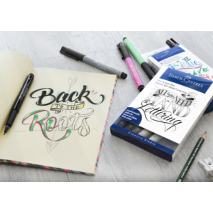 Set aus Tuschestiften auf einem Tisch mit einer geöffneten Skizze und einem Hand Lettering Booklet.