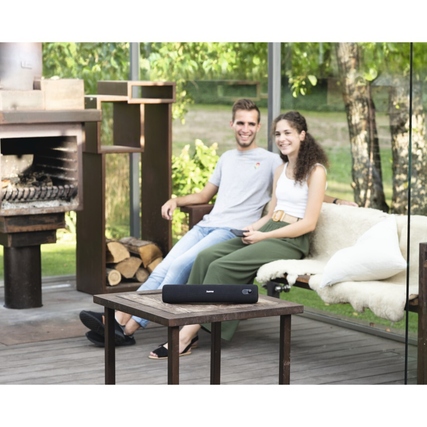 Bluetooth-Lautsprecher auf einem Tisch, umgeben von einer Sitzecke im Freien.