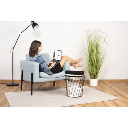 Bluetooth-Lautsprecher auf einem Tisch neben einem entspannten Nutzer im Raum.