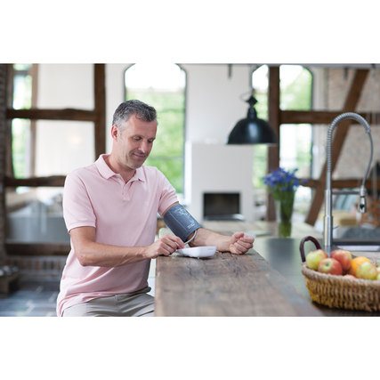 Oberarm-Blutdruckmessgerät wird von einer Person in einer modernen Küche verwendet.