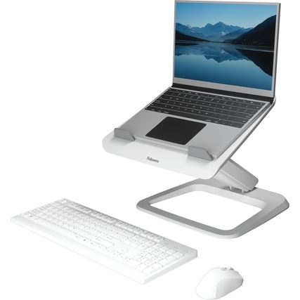 Weißer Laptopständer mit aufgeklapptem Laptop, daneben eine Tastatur und eine Maus auf einem Tisch.