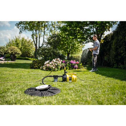Gartenpumpe mit Schlauch und Zubehör im Einsatz auf einer Rasenfläche mit Pflanzen im Hintergrund.