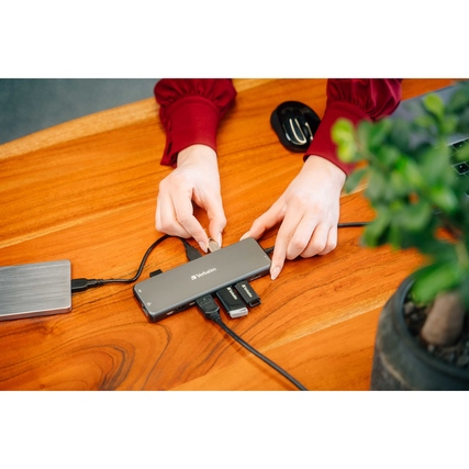 USB-Hub mit mehreren Anschlüssen wird von zwei Händen an einen Laptop angeschlossen.
