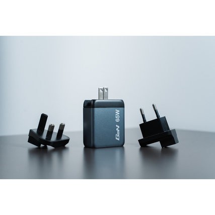 GaN-Ladegerät mit US-Stecker und austauschbaren EU- und UK-Steckern auf Tischfläche.
