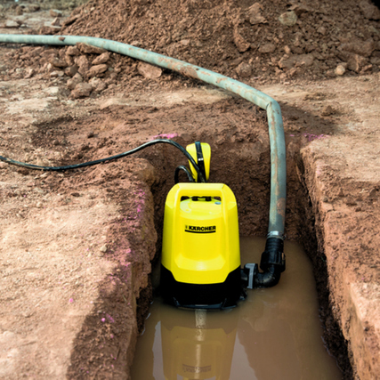 Wasserschlauch neben einer Pumpe in einer mit Wasser gefüllten Grube.