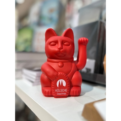 Rote Dekorationsfigur mit erhobener Pfote und Glücksmünze auf einem Regal.